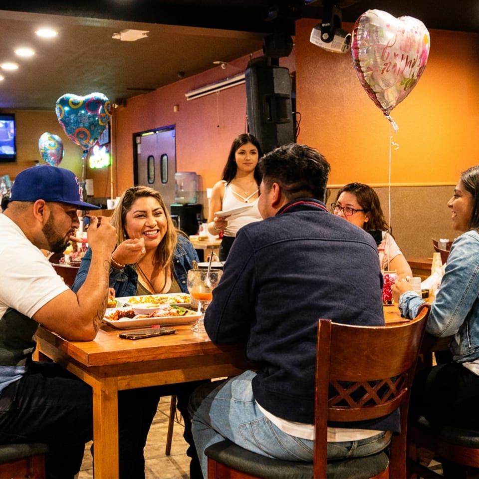 Group of friends and family enjoying a meal together at a lively restaurant with balloons.