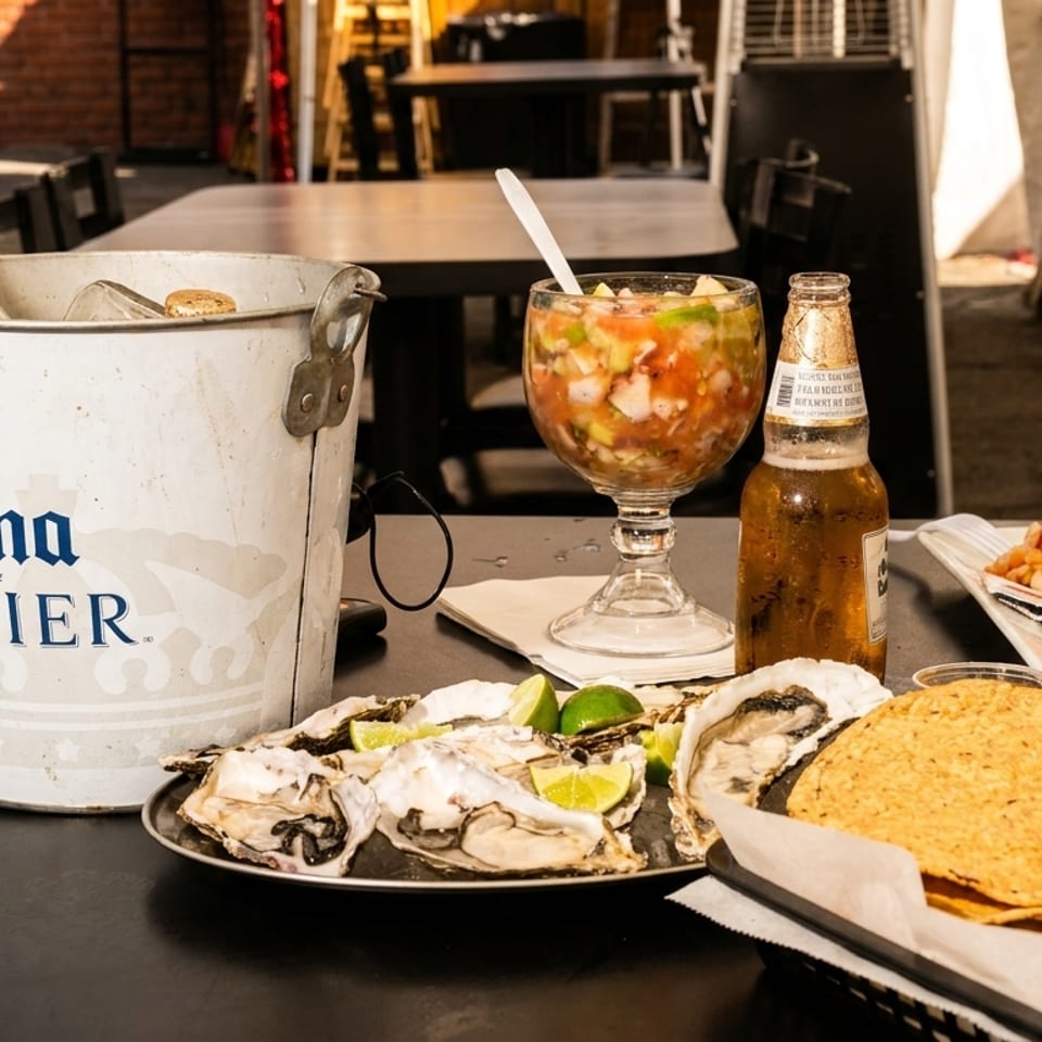 A table laden with oysters, ceviche, tostadas, and a bucket of Corona beers on an outdoor patio.