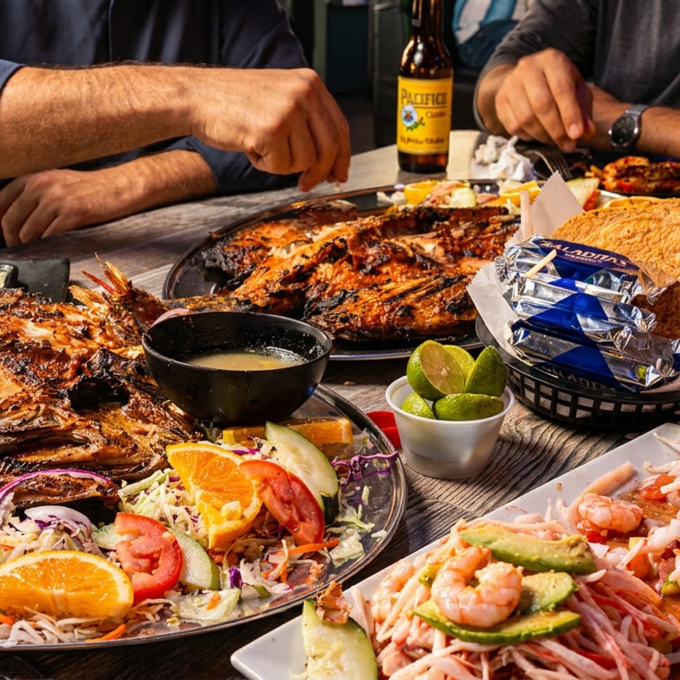 A table laden with grilled whole fish, ceviche, tortillas, and beer, with people dining.