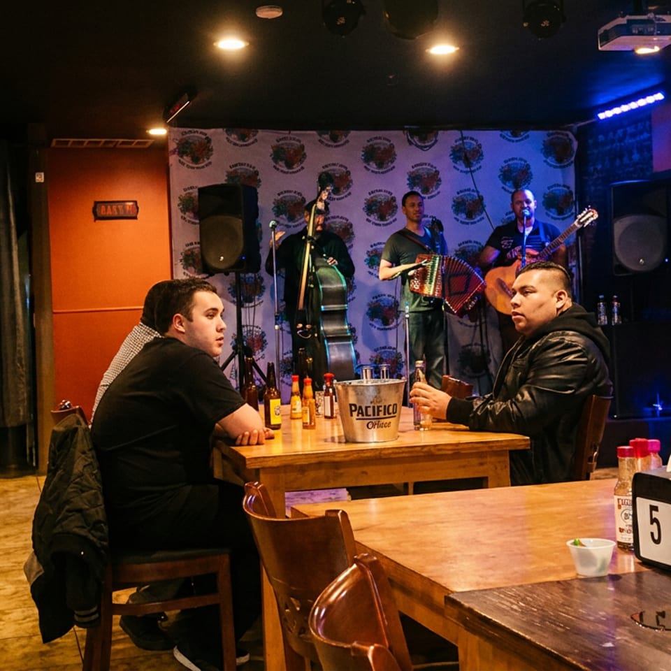 Diners at wooden tables watch a live band with a bass, accordion, and guitar in a restaurant.