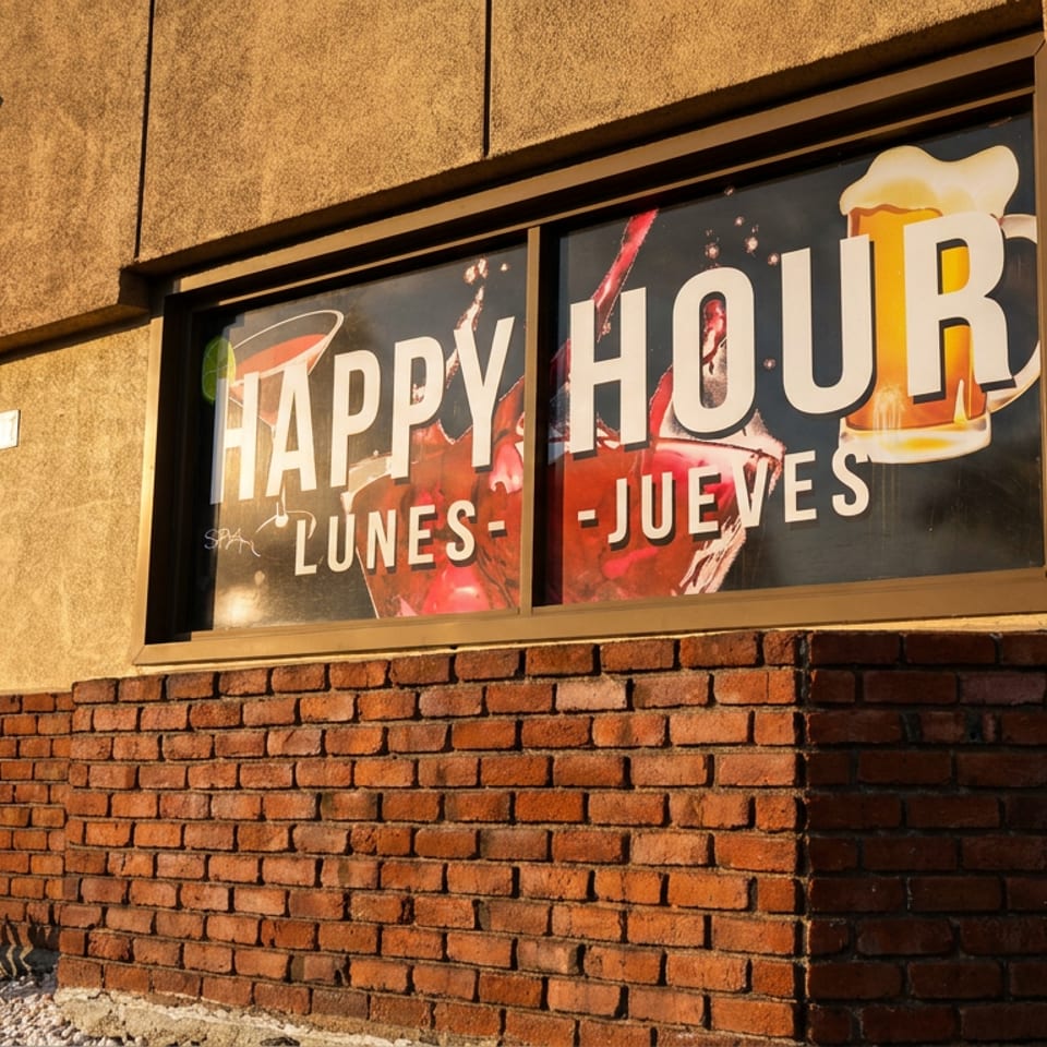 Restaurant window with a "Happy Hour Lunes - Jueves" sign, featuring cocktails and beer.