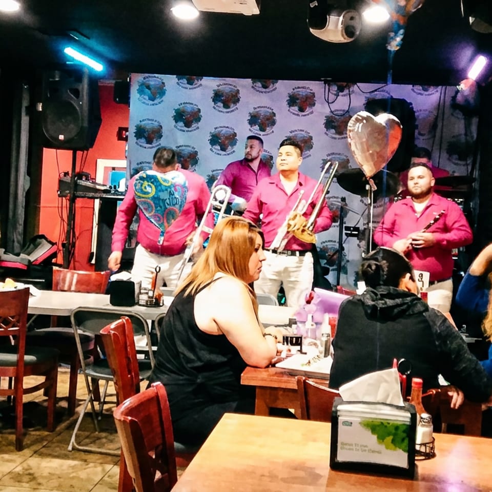 A band in pink shirts performs on stage for restaurant patrons seated at tables.